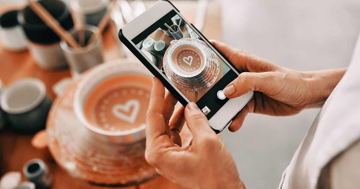 Hands capturing social media content photo of handcrafted bowl with heart design, representing brand consistency.